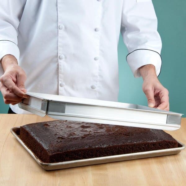 A chef holding a Baker's Mark half sheet cake pan with a chocolate cake on it.