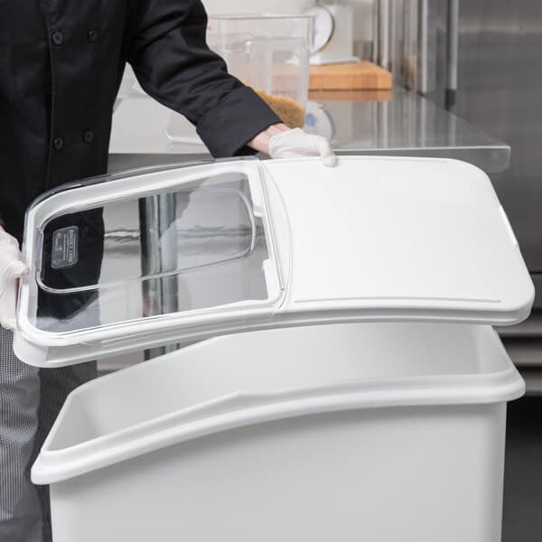 A man in a chef's uniform holding a white plastic container lid.