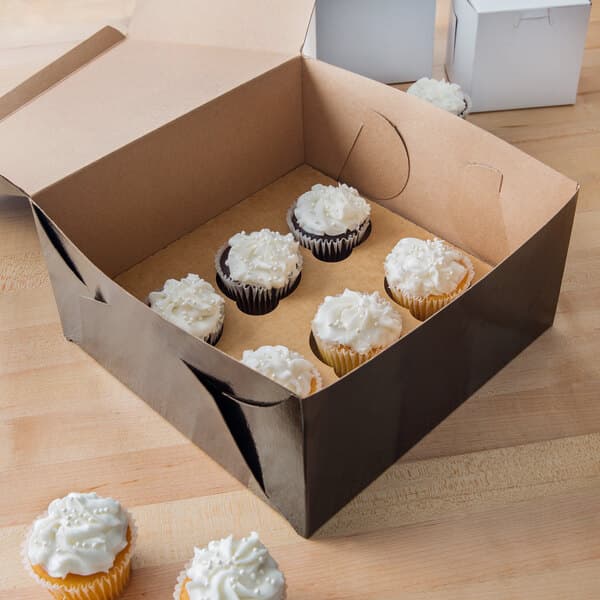 A Baker's Mark black cupcake box with a cupcake with white frosting and sprinkles inside.