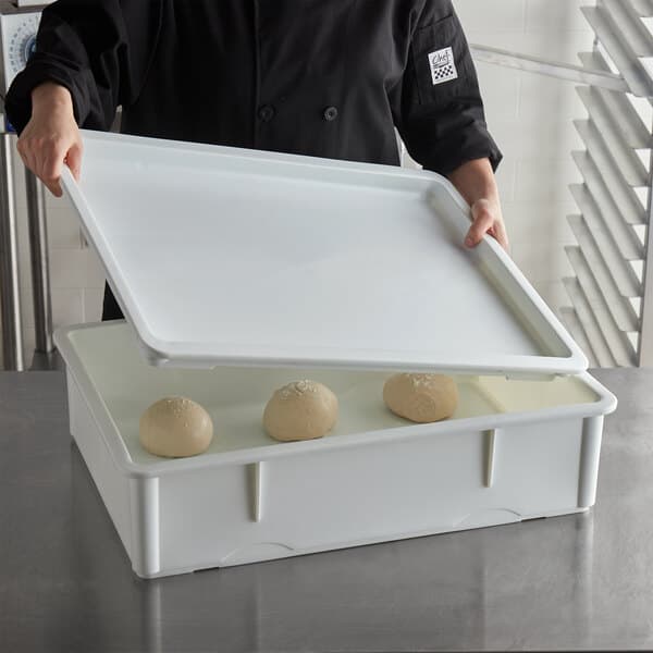 A person holding a white Baker's Mark dough proofing box lid with dough inside.