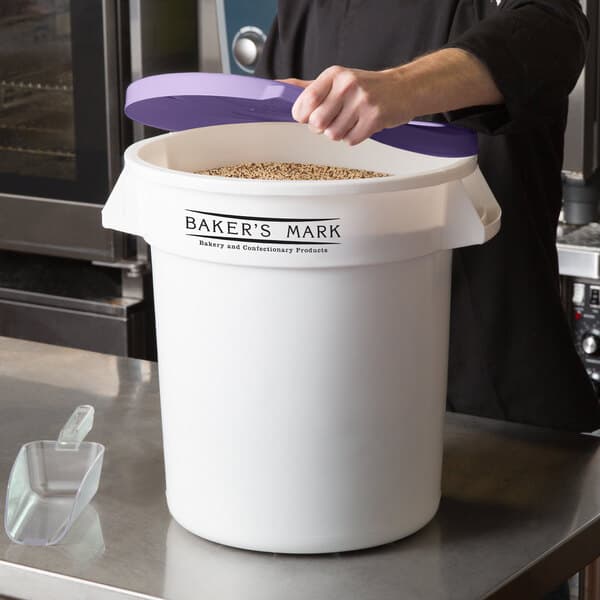 A person putting a purple lid on a white Baker's Mark ingredient storage bin.