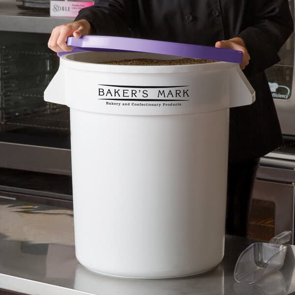 A woman holding a large white Baker's Mark ingredient storage container with a purple lid.