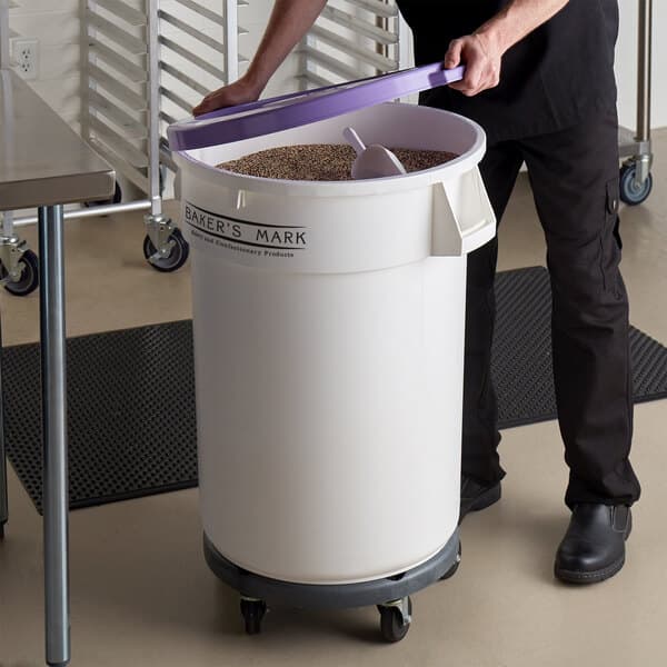 A man in a school kitchen using a Baker's Mark mobile ingredient storage bin with a purple lid to hold food.