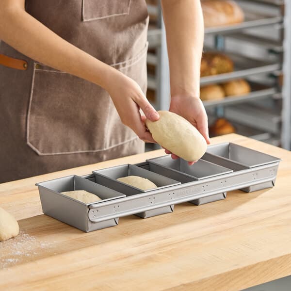 A four-compartment glazed aluminized steel bread loaf pan designed for baking multiple small loaves at once.