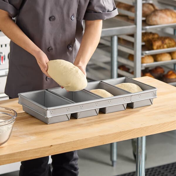 A four-compartment glazed aluminized steel bread loaf pan designed for baking multiple loaves at once.