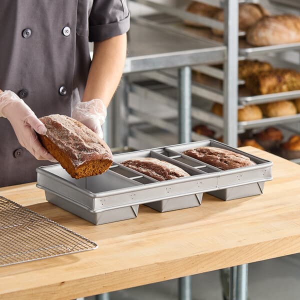 A three-compartment glazed aluminized steel bread loaf pan designed for baking 1 lb. loaves.