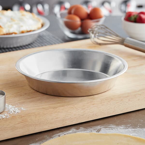 A close up of a Baker's Mark deep dish aluminum pie pan filled with a pie on a cutting board.