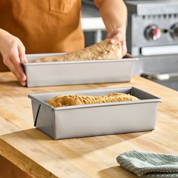 A rectangular glazed aluminized steel bread loaf pan measuring 10 by 5 by 3 inches, shown with a baked loaf inside.