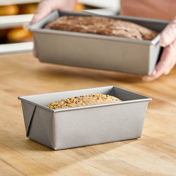A small rectangular glazed aluminized steel bread loaf pan filled with dough, placed on a wooden surface.