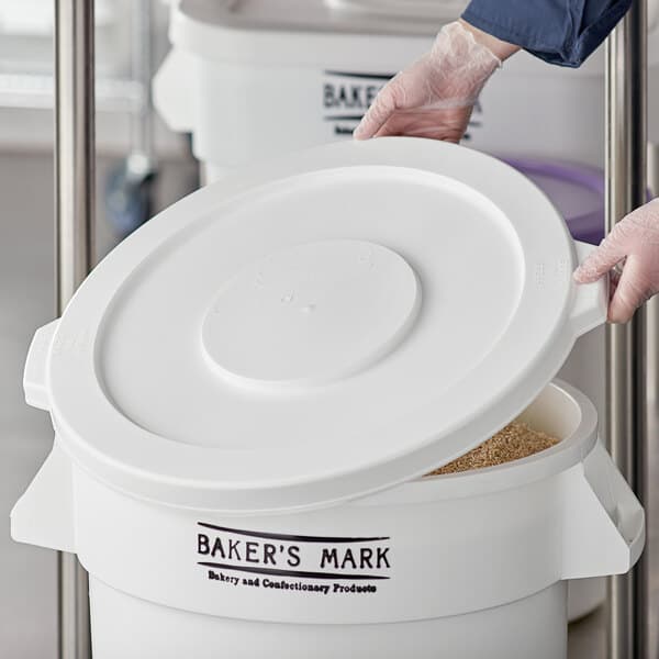 A person wearing gloves opens a white Baker's Mark ingredient bin lid.