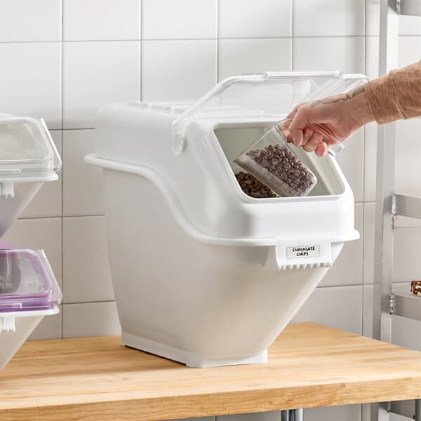 A white plastic ingredient bin with a flip lid, label sheet, and scoop, used for food storage.