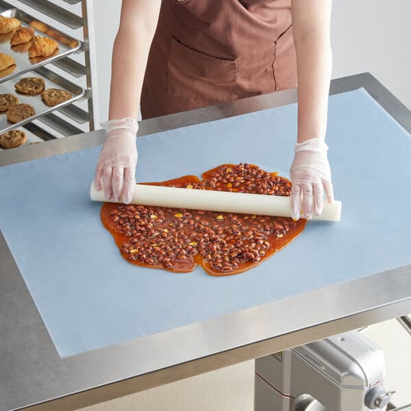 A person rolling out blue dough on a white silicone work mat.