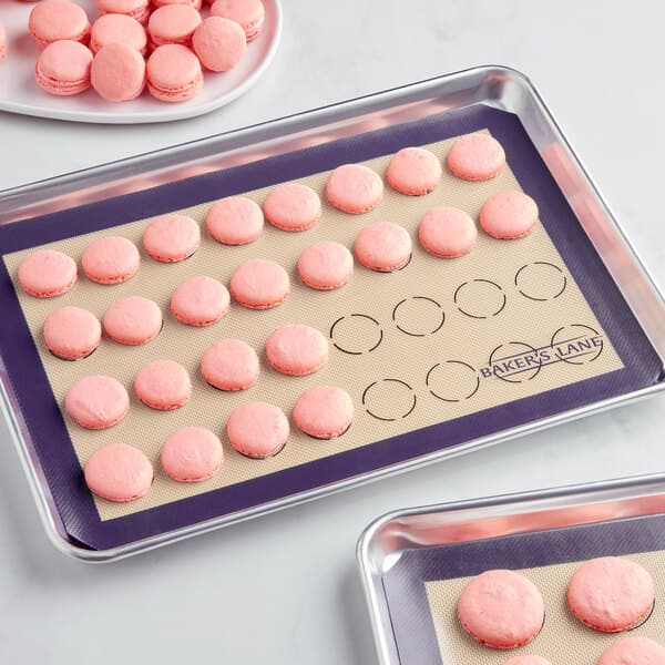 A tray of pink macarons baked with Baker's Lane purple silicone macaron baking mats on a white surface.