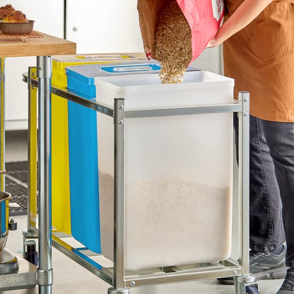 A white 10-gallon ingredient bin with a sliding lid, shown being filled with dry food in a kitchen setting.