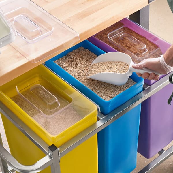 A person putting a scoop into a Baker's Mark yellow ingredient bin.