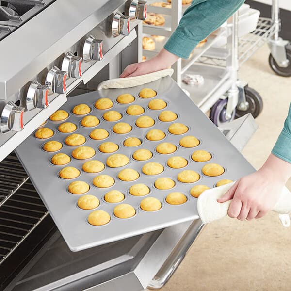 A person putting mini muffins into a Baker's Mark mini muffin pan.