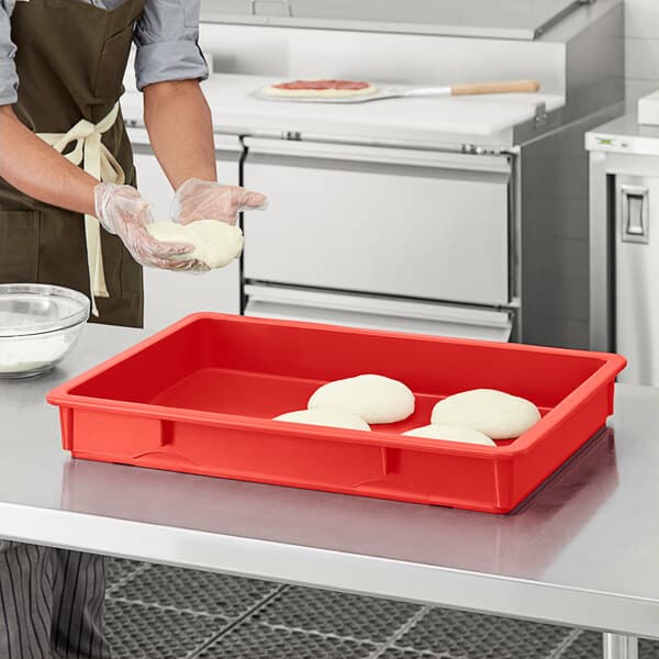 A person wearing gloves in a kitchen using a red Baker's Mark dough proofing box to hold dough.