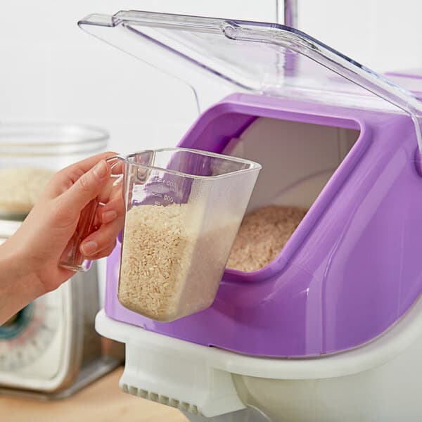 A hand using a clear plastic ice scoop to pour rice into a small glass container.