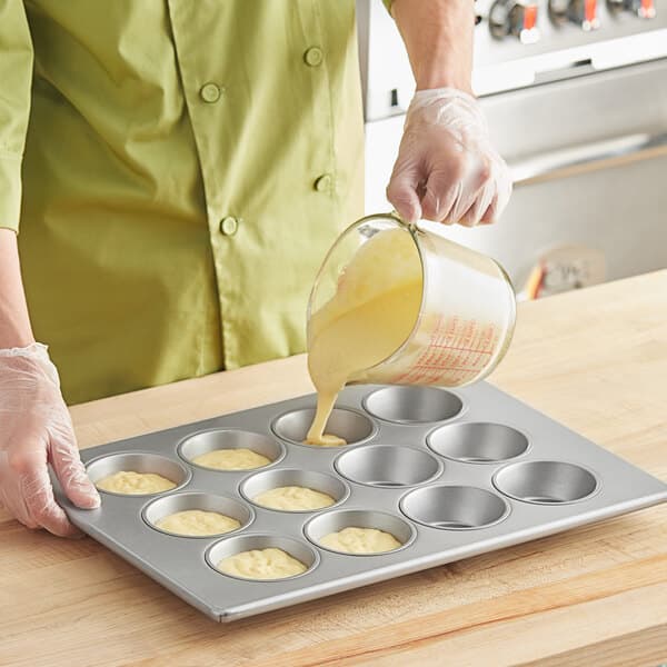 A person pouring batter into a Baker's Mark jumbo muffin pan.