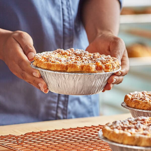 A person holding a Baker's Lane pot pie in a foil pan.
