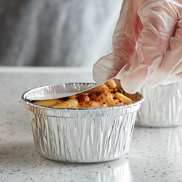 A close-up of food in a round foil ramekin with a board lid.