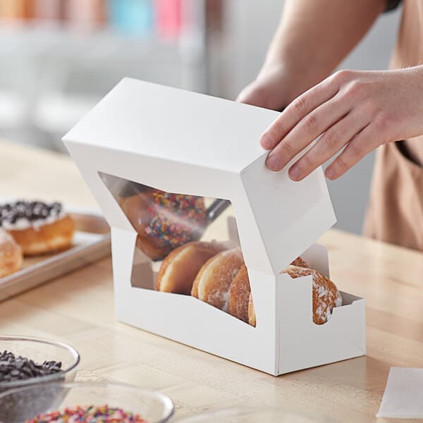 A white bakery box with a clear window, partially open and filled with assorted donuts.