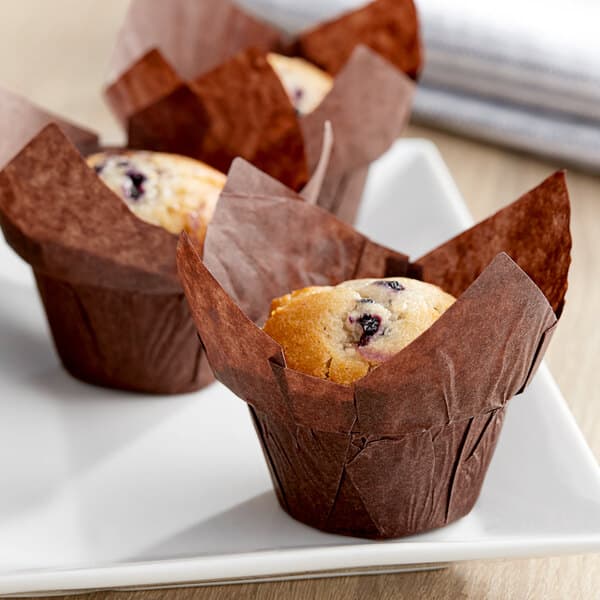 A medium-sized muffin in a chocolate brown high crown muffin wrap on a white plate.