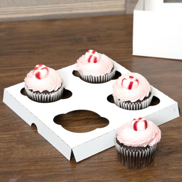 A Baker's Mark cupcake box holding four cupcakes with pink frosting and candy.