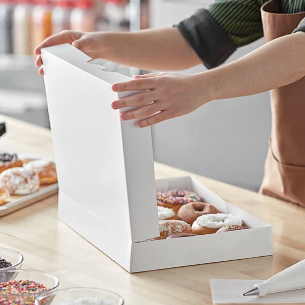 A person opening a white Baker's Mark bakery box of doughnuts.