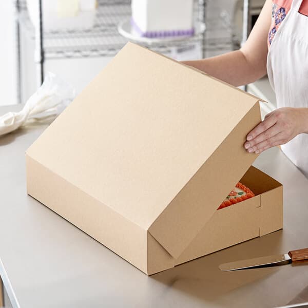 A woman opening a Baker's Mark kraft bakery box with a cake inside.