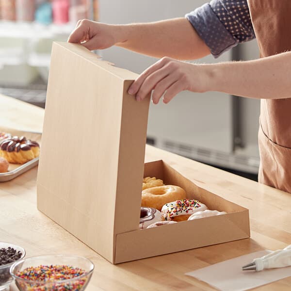 A woman opening a Baker's Mark Kraft bakery box to reveal donuts.
