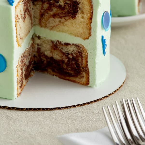 A slice of white cake with chocolate frosting and blue sprinkles on a Baker's Mark white cake circle.