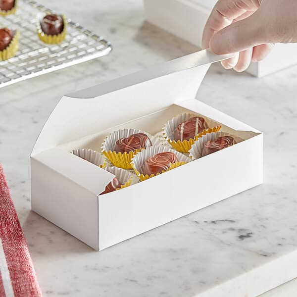 A hand putting chocolate into a white Baker's Lane candy box.