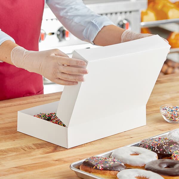 A woman opening a Baker's Lane box of donuts on a counter in a bakery display.
