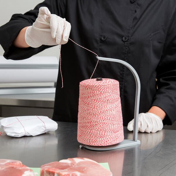 A person holding a spool of Baker's Mark red and white variegated twine.