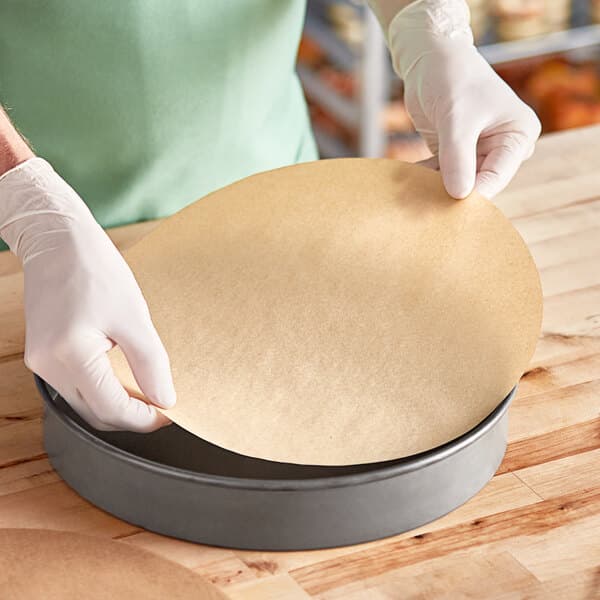 A person in gloves using a circular piece of Baker's Lane parchment paper.