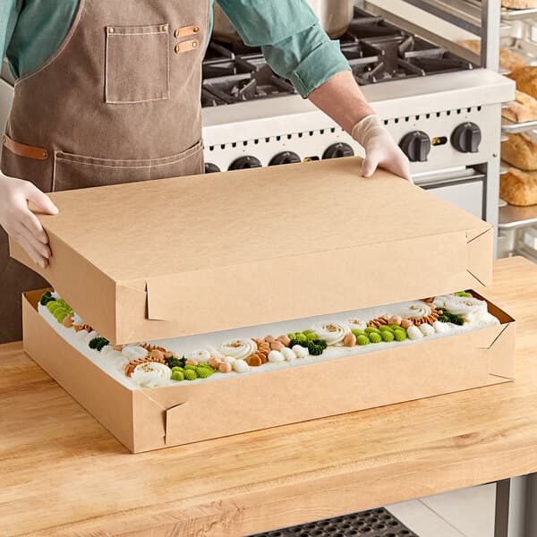 A man in a chef's uniform holding a Baker's Lane full sheet cake box.