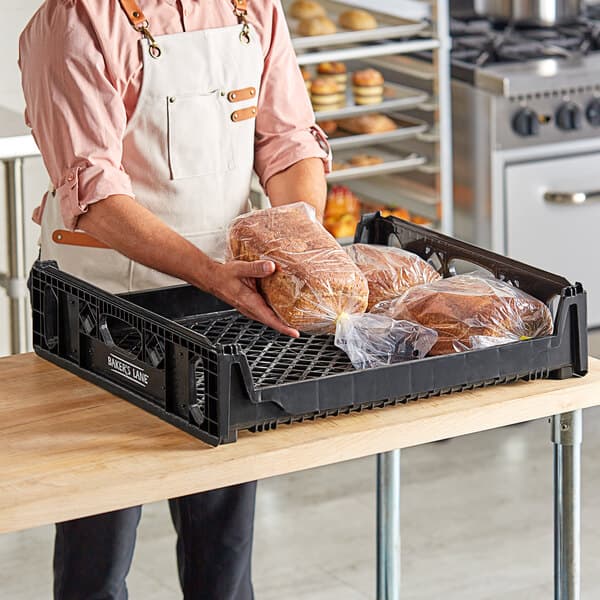 A man in an apron holding a black Baker's Lane bread tray with bread in it.