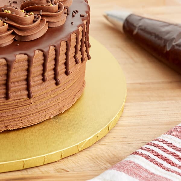 A Baker's Lane gold cake drum with a chocolate cake on a table with chocolate frosting and sprinkles.