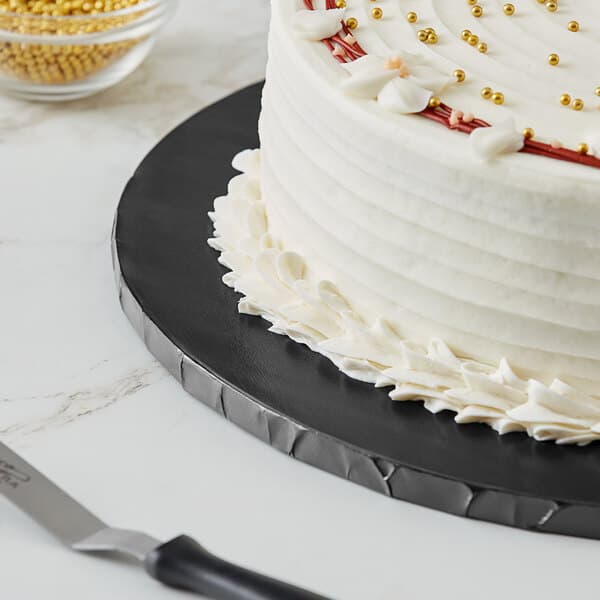 A Baker's Lane black cake drum with a cake on a plate next to a knife.