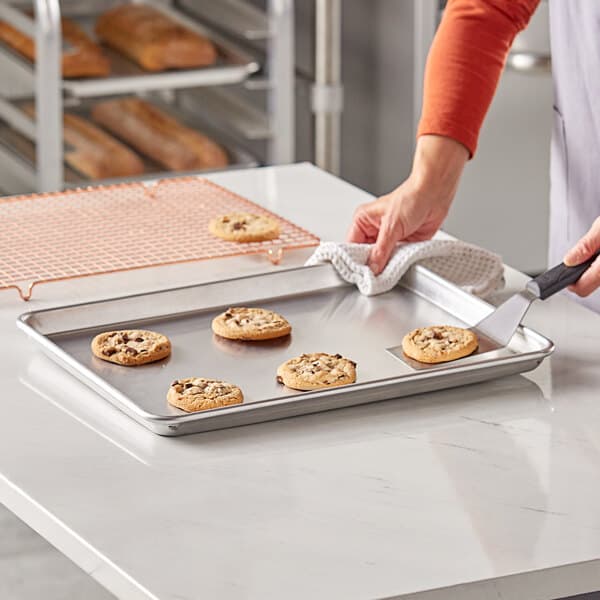 A person using a spatula to put cookies on a Baker's Lane USA aluminum sheet pan.