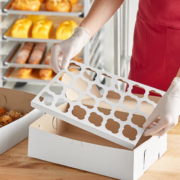 A person holding a white box with holes in it filled with mini muffins.