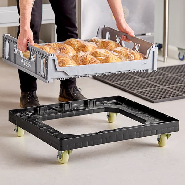 A person holding a black Baker's Lane bread tray on a black dolly.