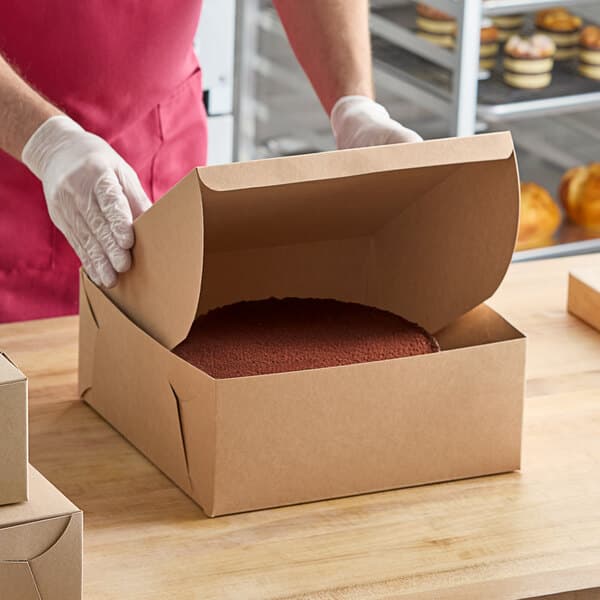 A person in gloves opening a Baker's Lane cake box.