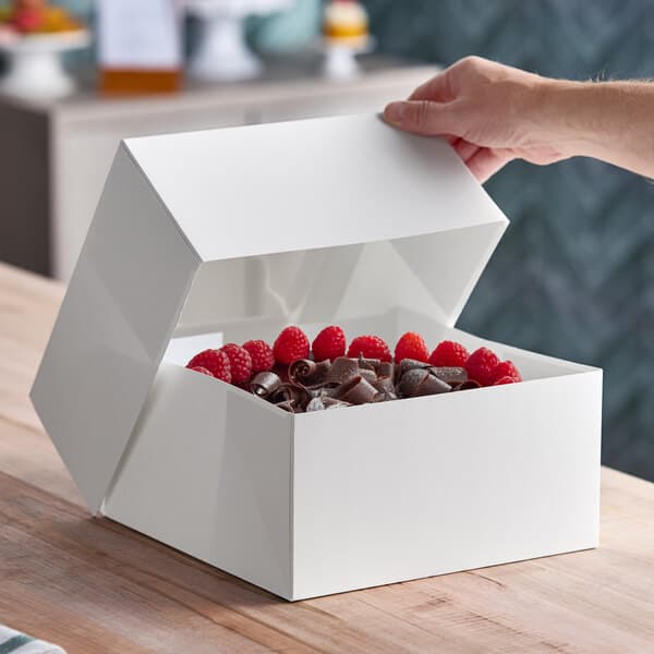 A white auto-popup bakery box containing a cake topped with raspberries and chocolate shavings.