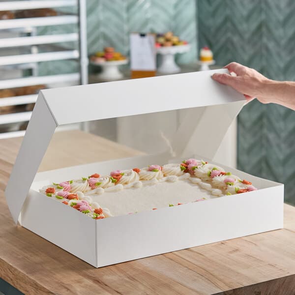 A large white auto-popup bakery box with a clear window, containing a decorated sheet cake.