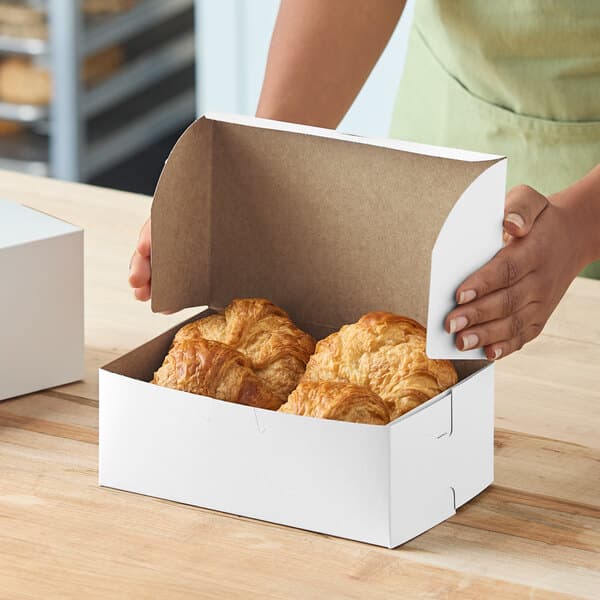 A white bakery box containing croissants being closed by a person.