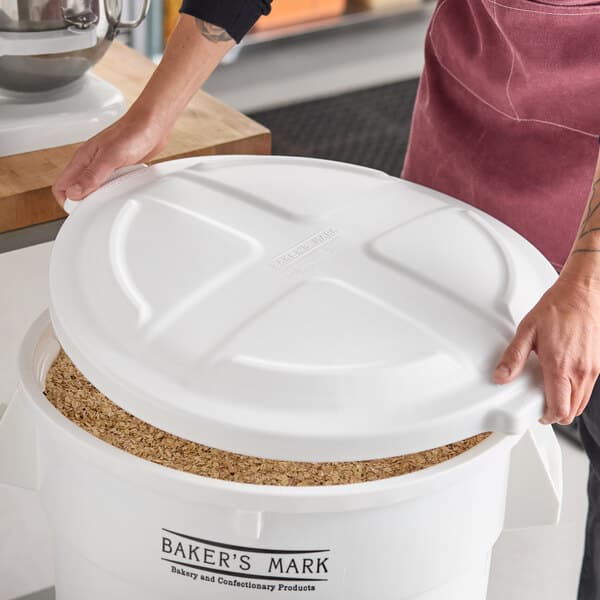 A white round dome lid being placed on a large Baker's Mark ingredient bin filled with oats.